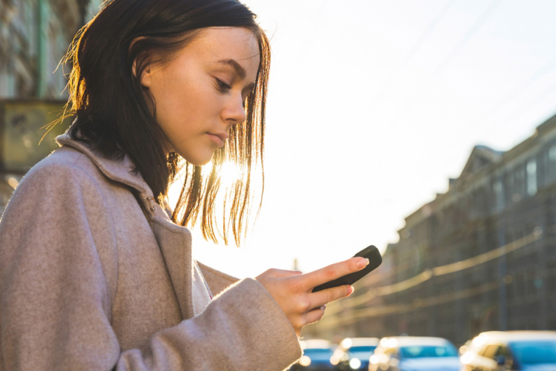 Woman using a smartphone outdoors to access Volkswagen electric vehicle charging app.