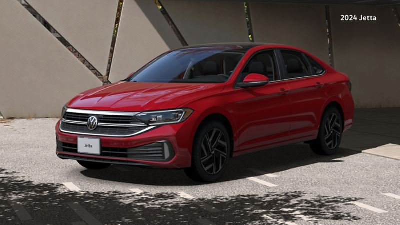 A three-quarter view of a 2024 Kings Red Metallic Jetta that is parked in a lot, underneath an architectural structure with a modern geometric design. The scene is sunny, casting shadows of the structure and nearby trees onto the concrete.
