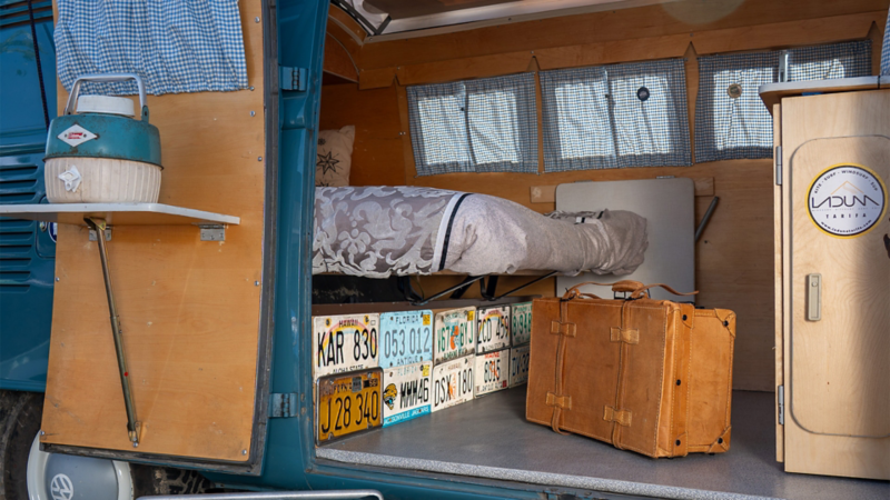 El interior de una VW T1, decorada con matrículas, una maleta y una cama.