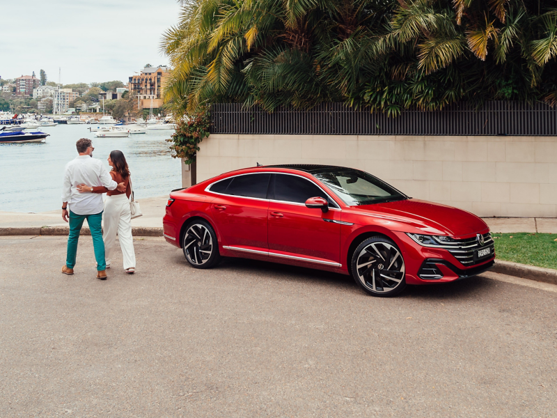 Couples walking beside new Arteon parked along river bank.