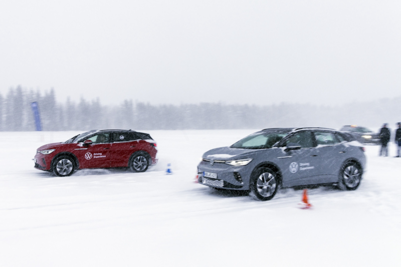 Två Volkswagen-bilar kör på en snötäckt isbana med koner i vintermiljö