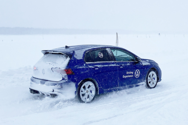 En blå Volkswagen Golf R kör på en snötäckt isbana i vintermiljö.
