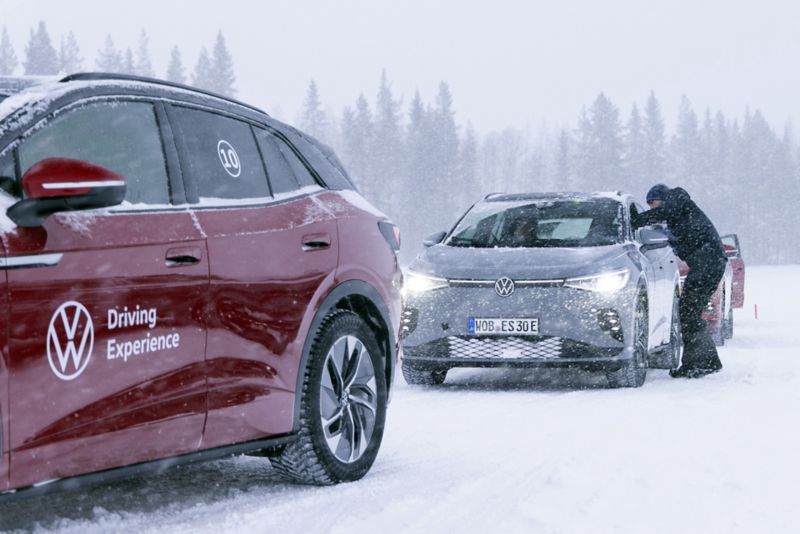 En röd och en grå elbil står parkerade efter varandra i ett vinterlandskap