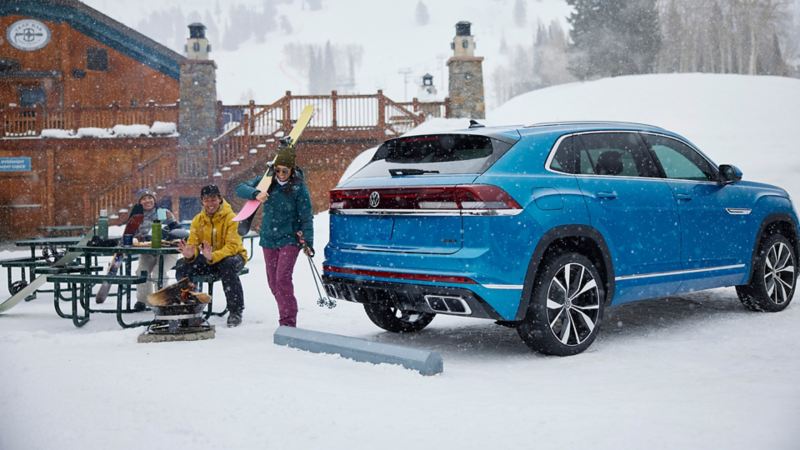 The blue 2024 Volkswagen Cross Sport parked on the parking lot near a man and a woman with skiing equipment