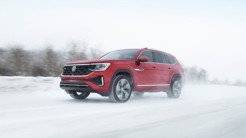 A close up photo of the red 2024 Volkswagen Atlas driving on the road covered with snow