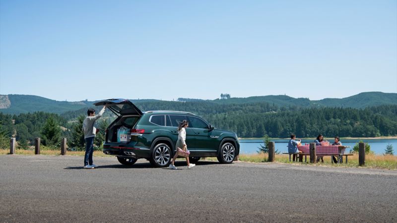 A man and a woman are unloading the 2023 Atlas trunk for a picnic by the lake.