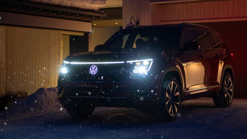 The 2024 Volkswagen Atlas at night parked near a garage during the winter featuring integrated LED light strip