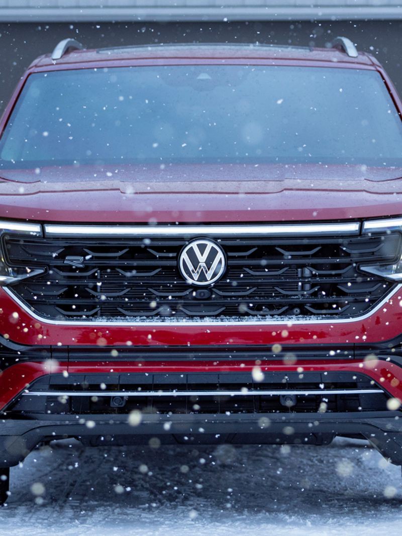 Une photo vue de face du Volkswagen Atlas 2024 rouge garé près d’un garage