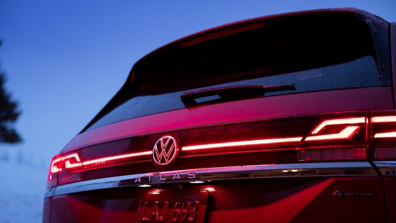 Une photo de vue arrière du Volkswagen Atlas 2024 rouge la nuit pendant l'hiver avec une bande lumineuse rouge à LED intégrée