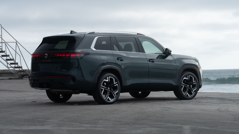 Vue trois quarts arrière d'un VUS Volkswagen Atlas vert foncé garé près d'une plage par temps couvert.  