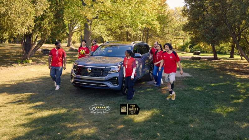 The pure grey Atlas Execline in a park, with a group of people in red soccer jerseys walking away, one holding a football.