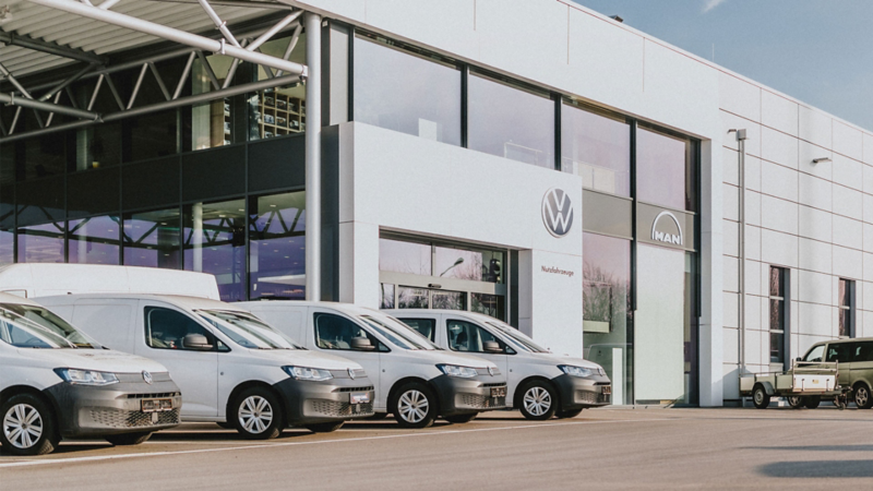 Le bâtiment de la concession Volkswagen "Garage Losch Truck, Van & Bus" à Niederanven présente plusieurs vans blancs garés devant.