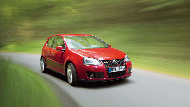 a red original Golf GTI driving down a countryside road