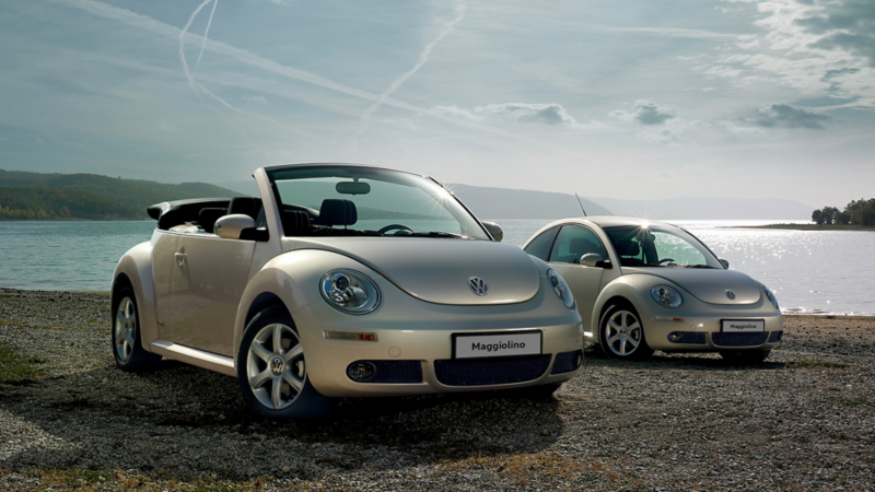 Vista 3/4 di New Beetle e New Beetle Cabriolet VW parcheggiati in una spiaggia.