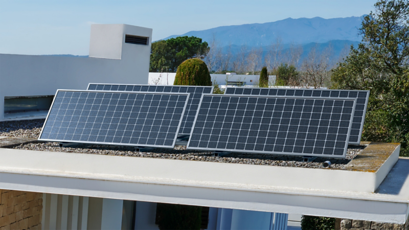 Photovoltaikanlage auf dem Flachdach eines modernen Hauses mit Blick auf bewaldete Hügel.