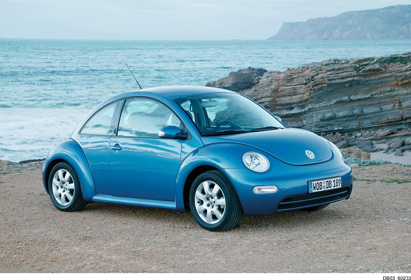 Blue Volkswagen Beetle parked on a coastal road with rocky cliffs and ocean in the background
