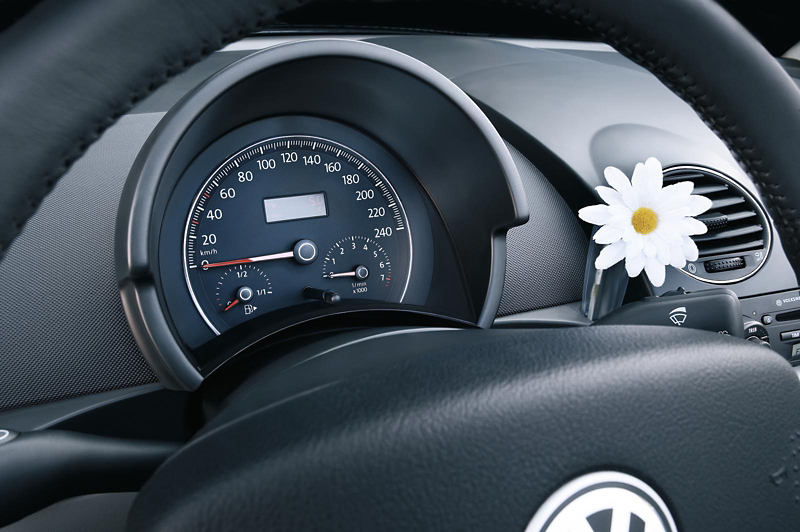 Inside a Volkswagen Beetle showing the steering wheel and analogue instrument cluster with speedometer and dashboard controls