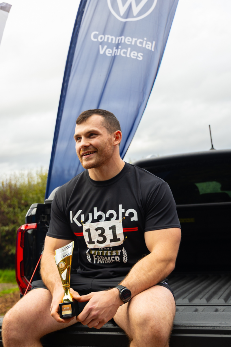 a pleased looking man looks into the distance whilst on the back of a van holding a trophy