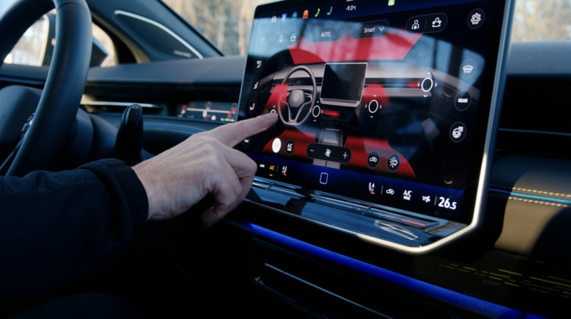 Närbild på bilens mittdisplay där en hand pekar på skärmen för inställningar och funktioner i en Volkswagen ID.7.