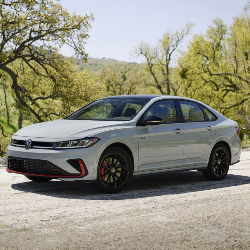 White Jetta GLI 2025 parked on a scenic road with trees and grassy hills in the background.