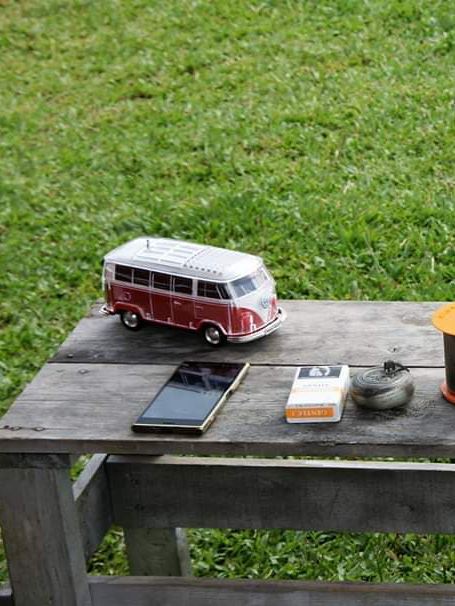 車主露營的桌面擺設，木製露營桌上擺有紅白雙色California 模型車、簡易水煮壺、鋼杯、手機和菸包