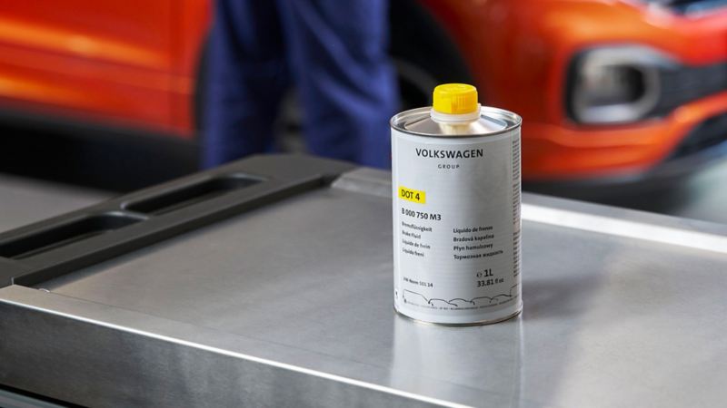 Can of Volkswagen Genuine Brake Fluid on a roller container, a VW T-Cross in the background