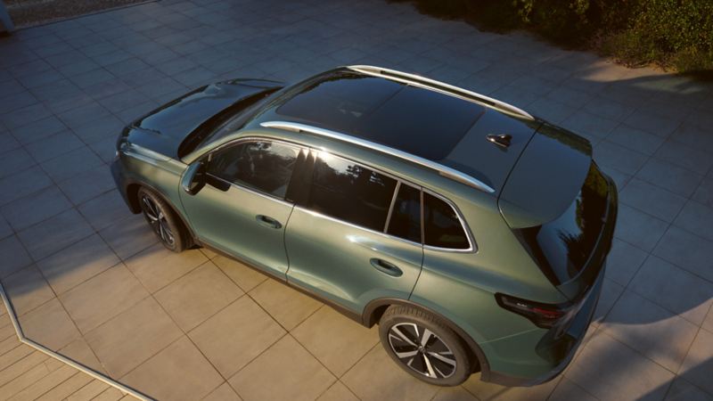 A young man smilingly walks away from a green Tiguan towards a young woman, who joyfully awaits him.