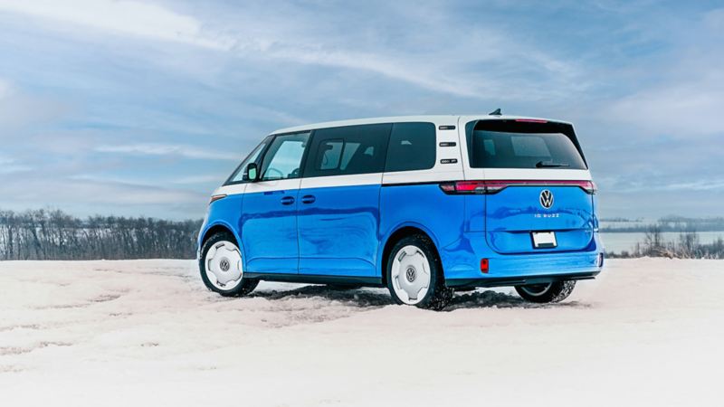 A blue and white Volkswagen ID. Buzz parked in a snowy landscape.