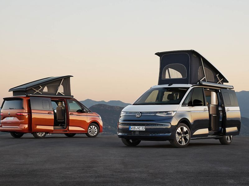 Deux VW California côte à côte avec le toit relevable relevé et les portes coulissantes ouvertes.