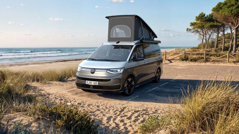 VW California mit ausgefahrenem Aufstelldach steht auf einem Parkplatz am Strand.