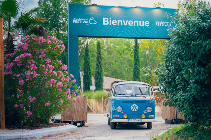 un van T2 passe sous l'arche California village du california festival vw volkswagen 2025