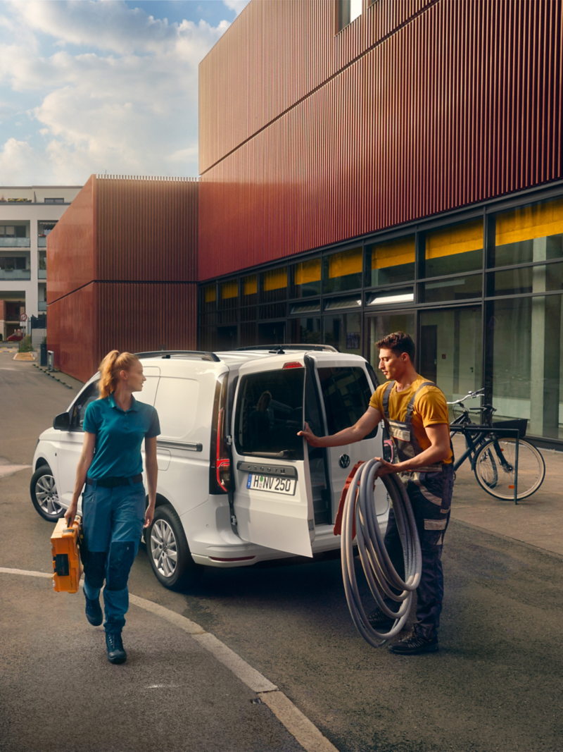 Zwei Handwerker laden ihr Material und Werkzeug aus dem VW Caddy Cargo.