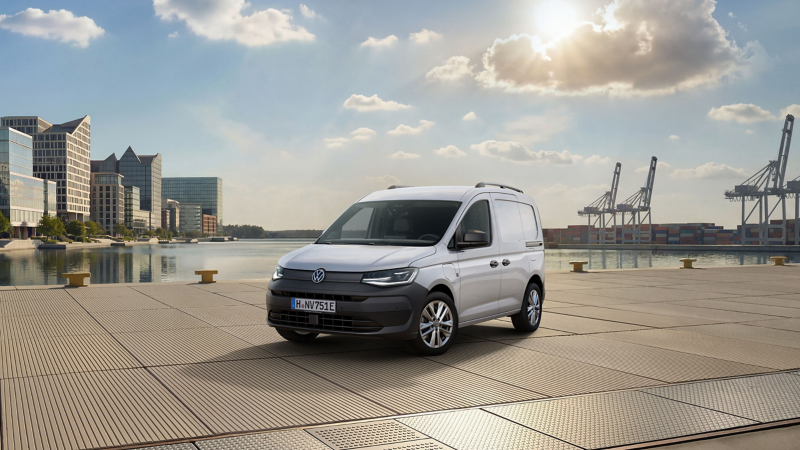 Ein VW Caddy Cargo eHybrid steht am Wasser, im Hintergrund befindet sich ein Hafen und eine Stadt.