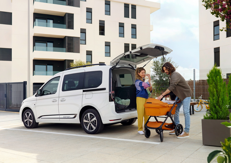 Der VW Caddy Edition mit geöffneter Heckklappe wird von einer Jungen Familie ausgeladen..