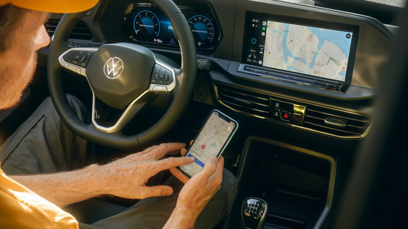 Eine Person mit einem Smartphone in der Hand sitzt auf dem Fahrersitz eines VW Nutzfahrzeug.