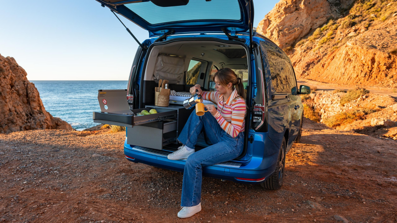 Die herausziehbare Miniküche in einem blauen VW Caddy California an einer Klippe am Meer