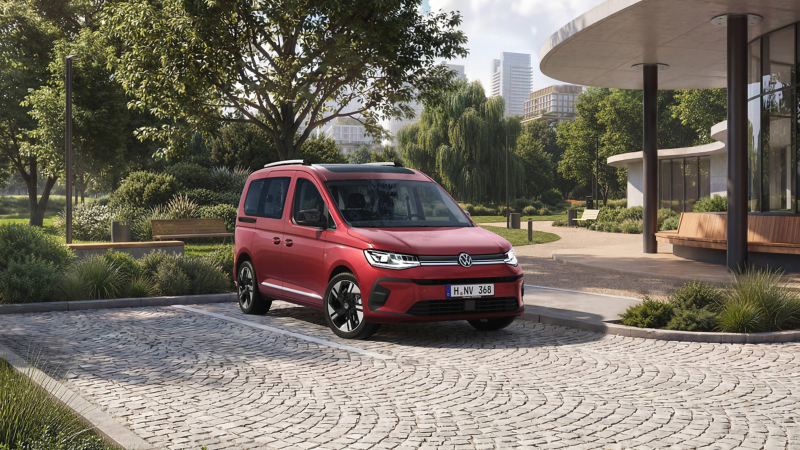 Roter VW Caddy steht auf einem Parkplatz vor einem Park in einer Stadt.