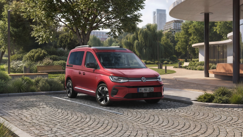 En röd VW Caddy Personbil står parkerad vid en park