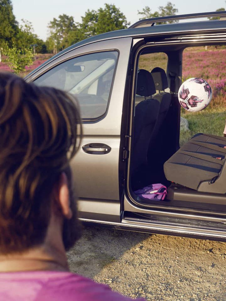 Un bambino lancia una palla attraverso la porta scorrevole aperta di Volkswagen Caddy Kombi.
