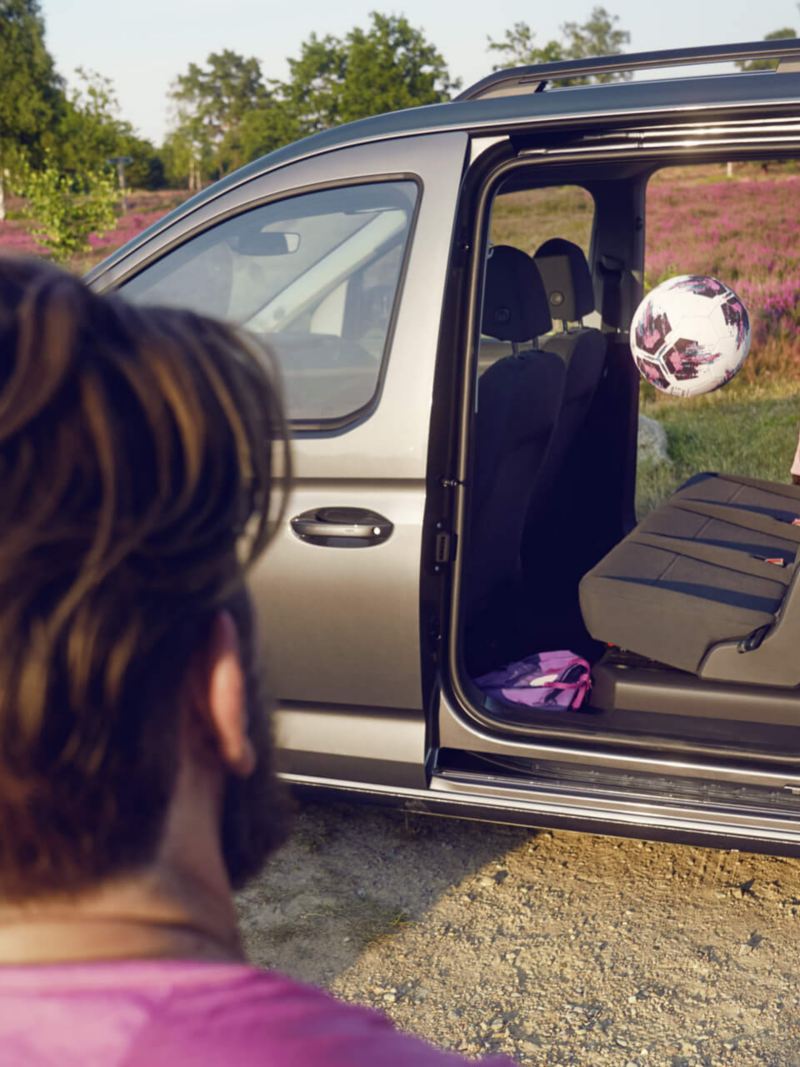 Un enfant jette un ballon par la porte coulissante ouverte du VW Caddy Combi. 