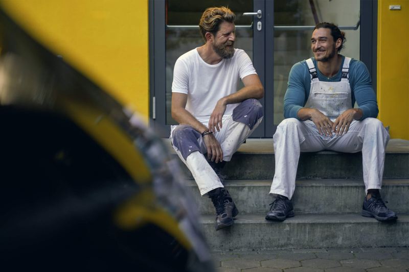 Zwei Maler sitzen auf einer Steintreppe und lachen.
