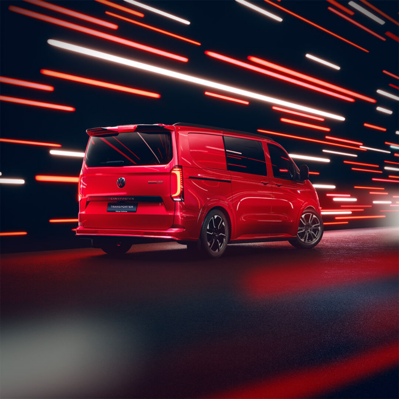 A sleek red Transporter Sportline van is driving under vibrant streaks of red and white lights, suggesting speed and motion. The scene conveys a futuristic and dynamic tone.
