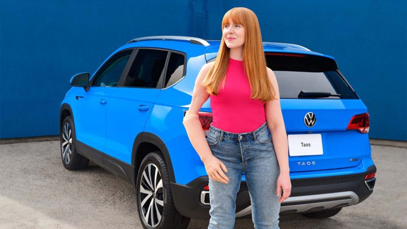 Une femme portant une prothèse au bras debout derrière le Volkswagen Taos 2022 bleu
