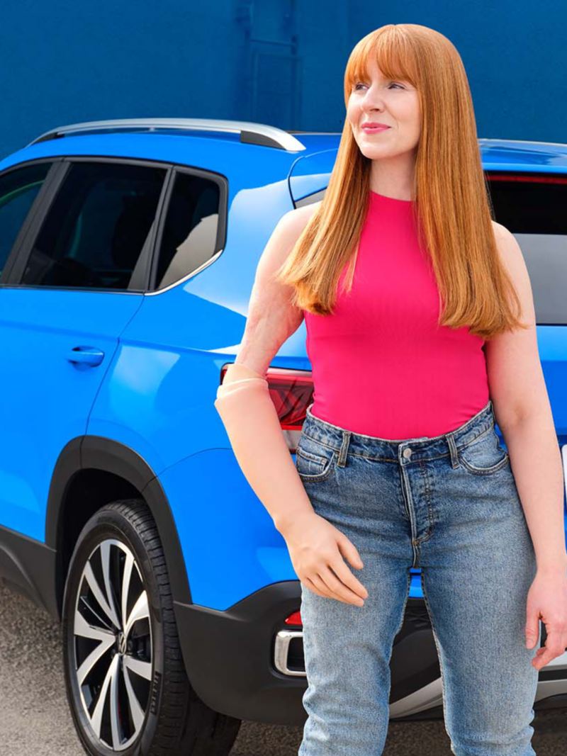 Une femme portant une prothèse au bras debout derrière le Volkswagen Taos 2022 bleu