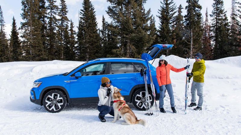 People are unloading skiing equipment from the 2022 Volkswagen Taos while looking at a woman who is kissing a dog 