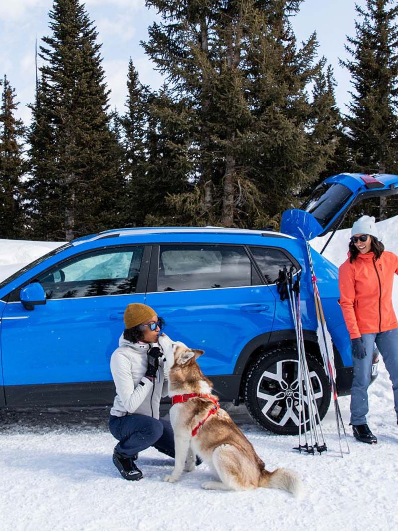 Des gens sortent de l'équipement de ski du Volkswagen Taos 2022 en regardant une femme qui embrasse un chien