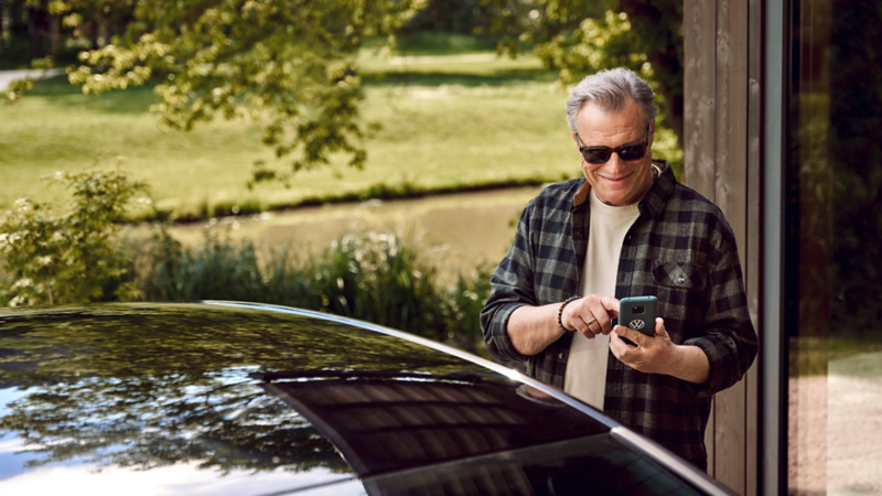 Älterer Mann schaut auf sein Handy vor dem Fahrzeug