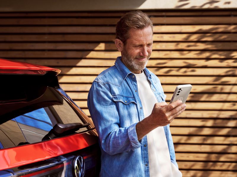 Mann schaut auf sein Handy vor seinem Volkswagen.