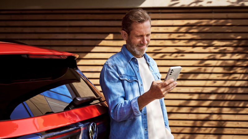 Mann schaut auf Handy vor seinem Volkswagen