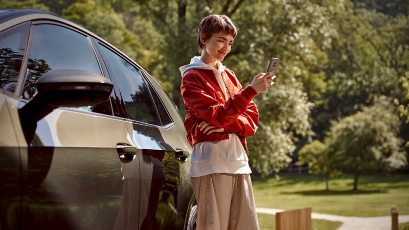 Kobieta stoi obok VW ID.3 i patrzy na swój smartfon.